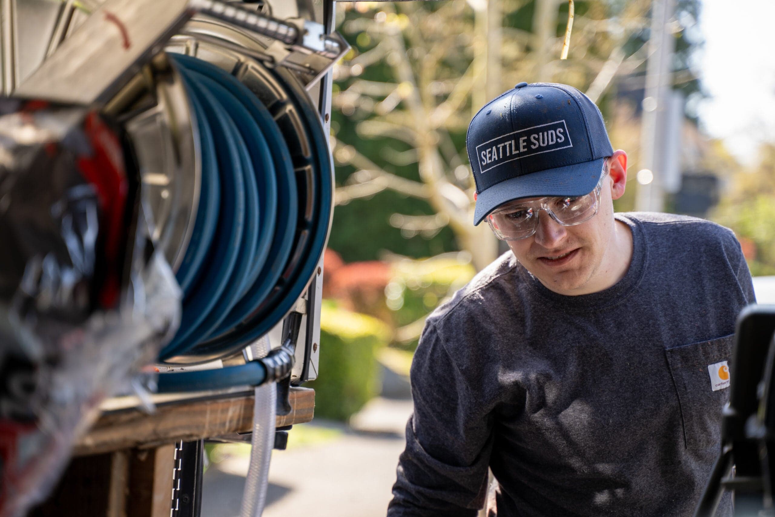 Seattle Suds crew member in a branded cap and safety glasses at the truck hose reel