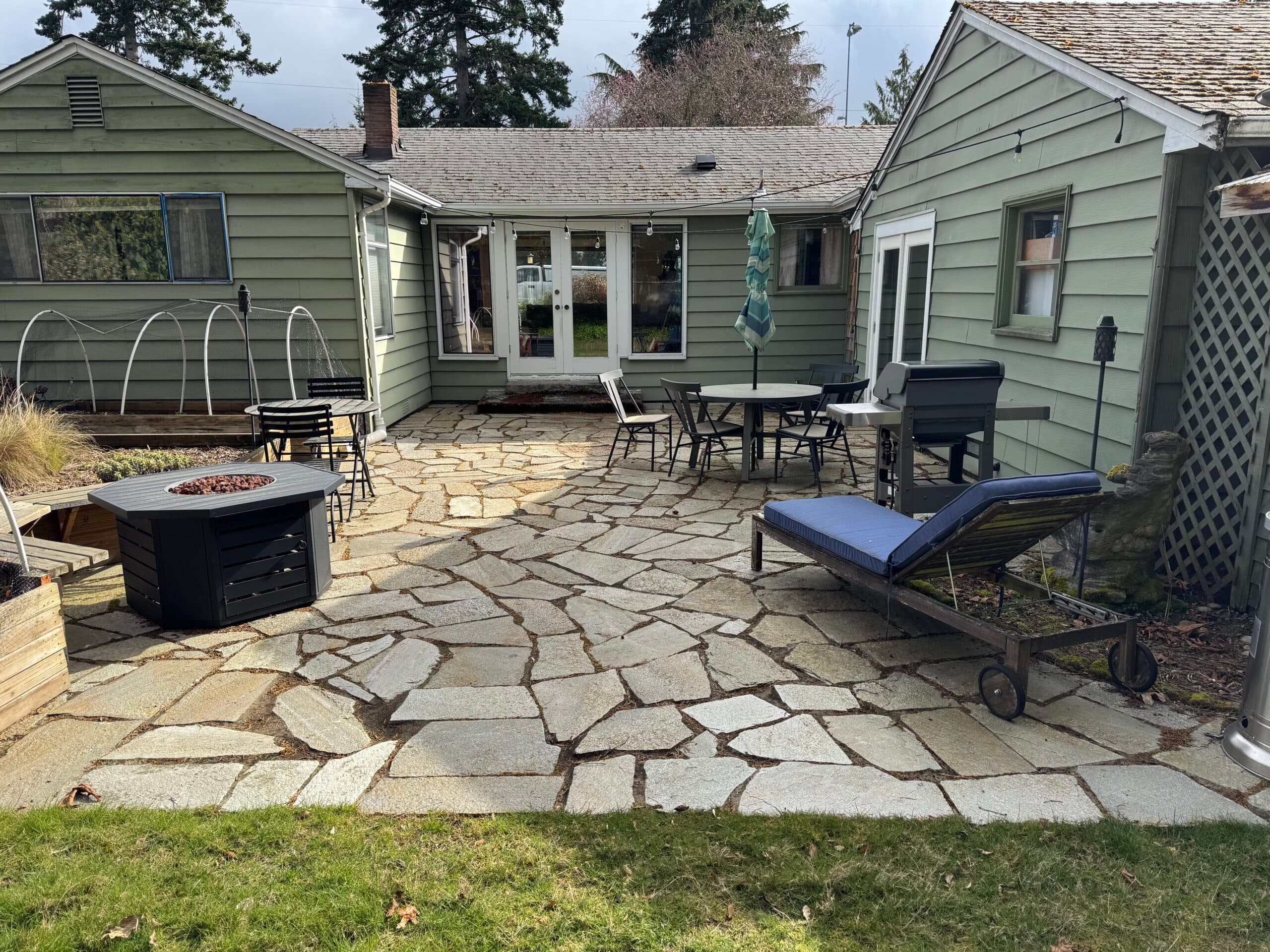 Clean flagstone patio with a fire pit in front of a sage-green home