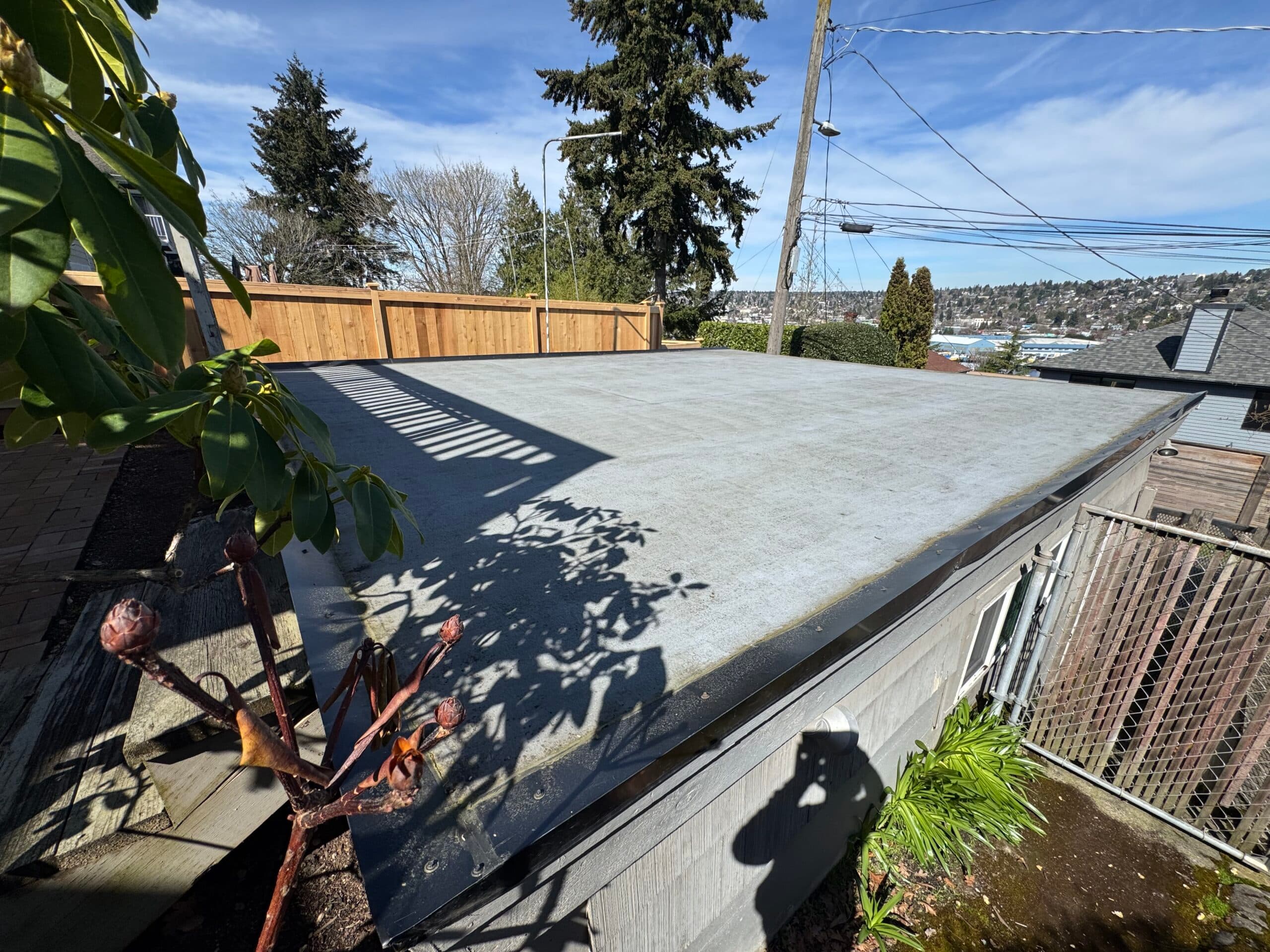 The same flat garage roof under blue sky with a Seattle hillside behind